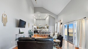 Una sala de estar moderna con un sofá de cuero negro, un comedor con mesa y sillas, y una cocina al fondo.