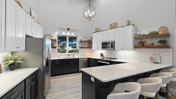 Una cocina moderna con armarios blancos, una isla central, taburetes de bar y una lámpara colgante.