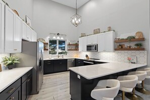 Une cuisine moderne avec des meubles blancs, un îlot central, des tabourets de bar et un luminaire suspendu.