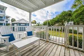 Une terrasse en bois, avec des chaises blanches et une table, donnant sur une pelouse et un bâtiment dont le toit est bleu.
