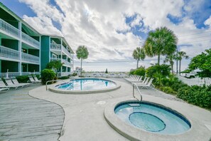 Un espace piscine comprenant deux bains à remous, des chaises longues et un bâtiment doté de balcons.