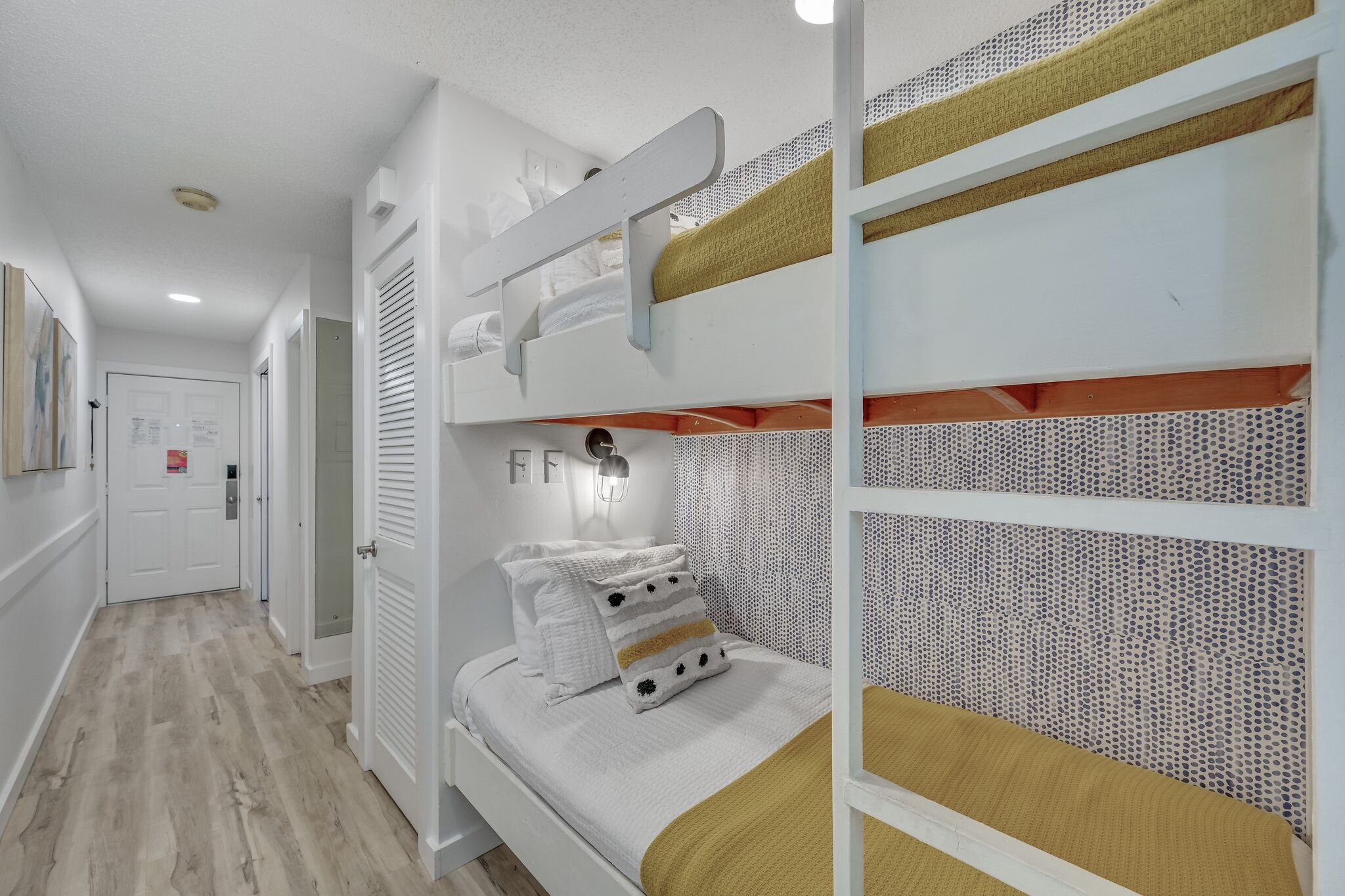 A bunk bed with a patterned headboard, a bedside table with a lamp, and a door with a lock.
