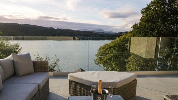 A terrace with a sofa, a table with a bottle and glass, and a view of a lake and mountains. - Kessock (Windermere)