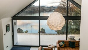 A modern interior with a large window offering a view of a lake and hills. - Kessock (Windermere)
