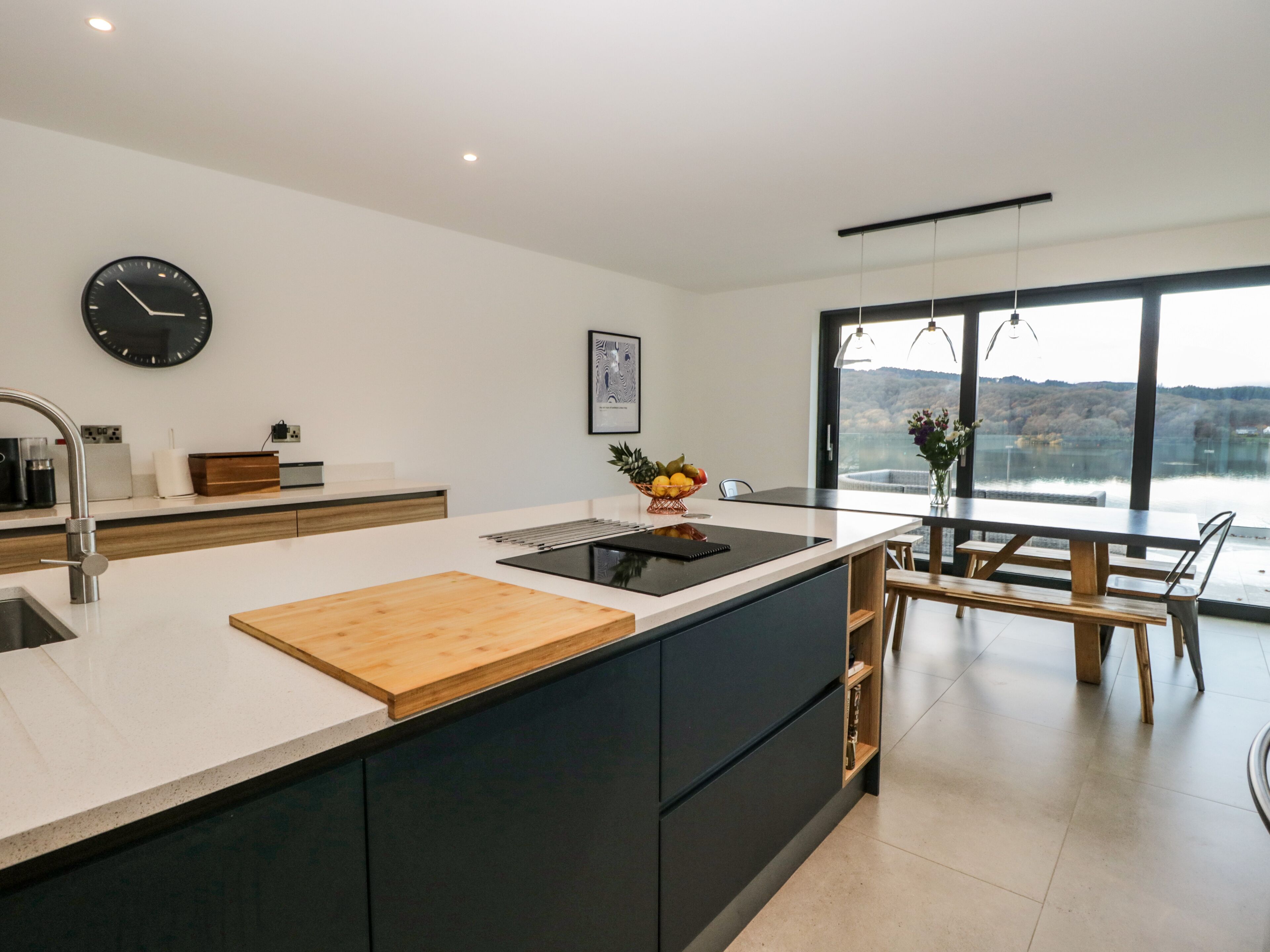 A modern kitchen with a large island, a dining area with a view, and a clock on the wall.