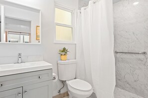 A bathroom with a white vanity, a toilet, a shower with a white curtain, and a marble wall.