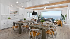 A modern kitchen with white cabinets, a wooden dining table, and a large window overlooking the ocean. - Prime Waterfront Retreat P807-2 (Oceanside)