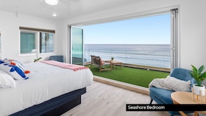A bedroom with a large bed, a view of the ocean, a balcony with a chair, and a small table. - Prime Waterfront Retreat P807-2 (Oceanside)