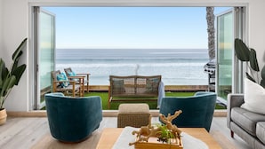 A modern living room with a view of the ocean, featuring wicker furniture, a grey sofa, and a wooden coffee table with decorative items. - Prime Waterfront Retreat P807-2 (Oceanside)