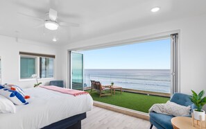 Une chambre avec un grand lit, une vue sur l’océan, un balcon avec une chaise et une petite table.