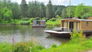 A lakeside cabin with a dock, surrounded by lush greenery and a forested backdrop. - Toue cabanée (Chamberet)
