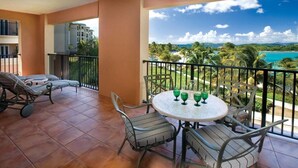 A balcony with a table and chairs, a view of a beach, and a building in the background. - Luxurious 2 bedroom, 2 bath Oceanfront Condo @ the Ritz Carlton Club (St Thomas)