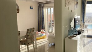 Ein großzügiger Wohnbereich mit Balkon, einem weißen Sofa, einem gemusterten Sessel und einem kleinen weißen Tisch mit Dekoration.