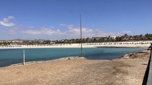 Eine Küstenlandschaft mit einem Sandstrand, blauem Himmel und einer Reihe blauer Liegestühle am Ufer.