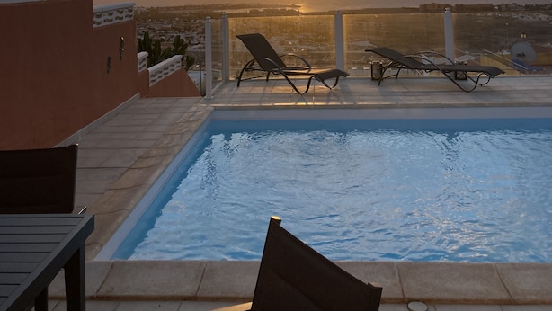 Ein Poolbereich auf dem Dach mit Liegestühlen und Blick auf den Sonnenuntergang über dem Meer.