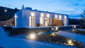 A modern house with a stone exterior, large windows, and a well-lit patio area. - Desire Mykonos Apartments (Mykonos)