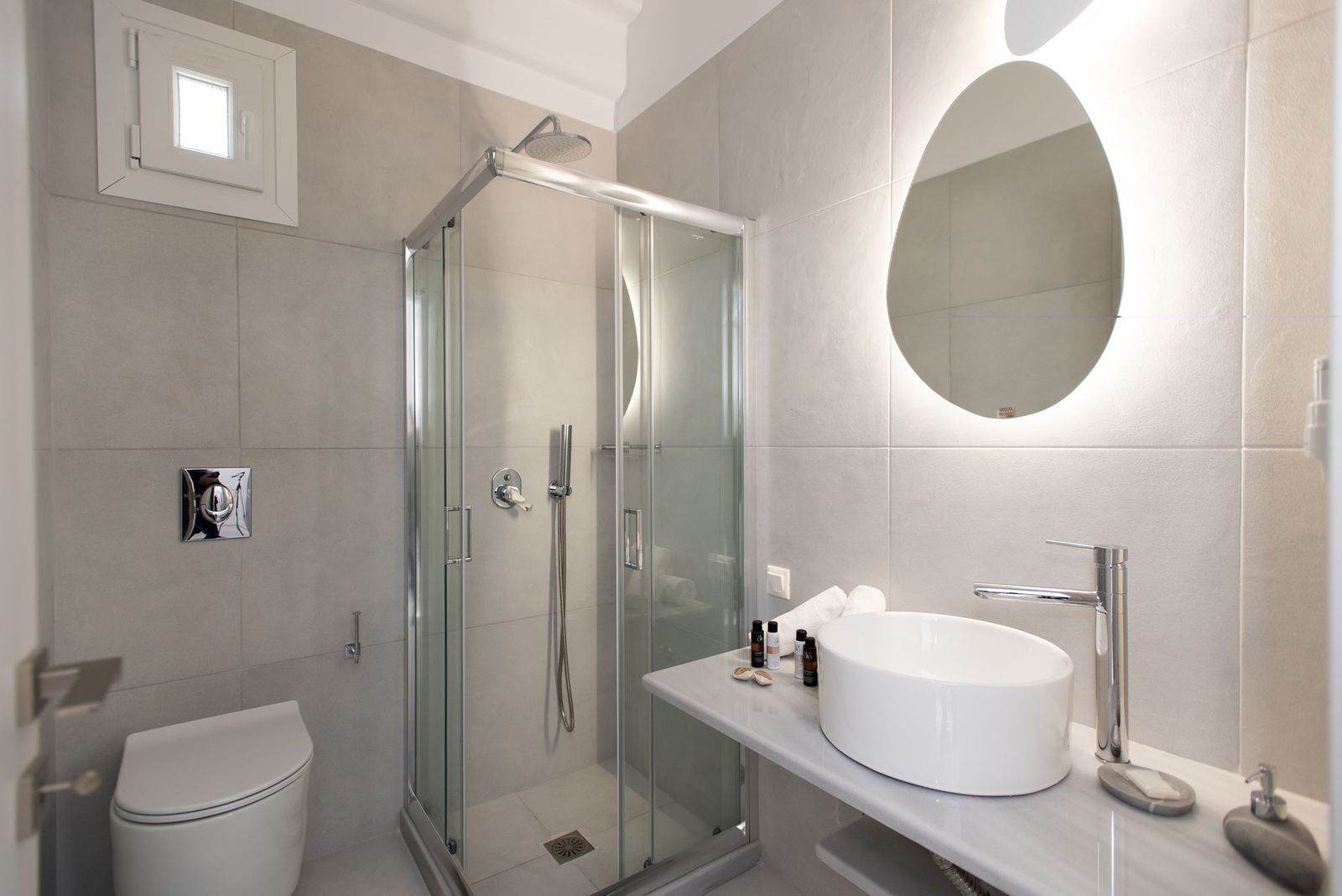A modern bathroom with a glass-enclosed shower, a white sink with a round mirror, and a toilet.