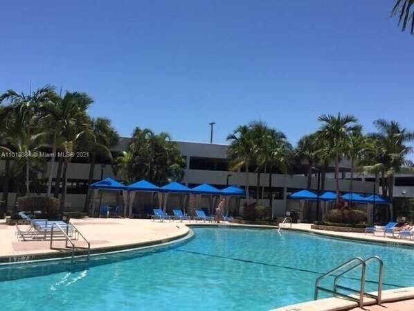 A swimming pool with blue umbrellas, palm trees, and lounge chairs.