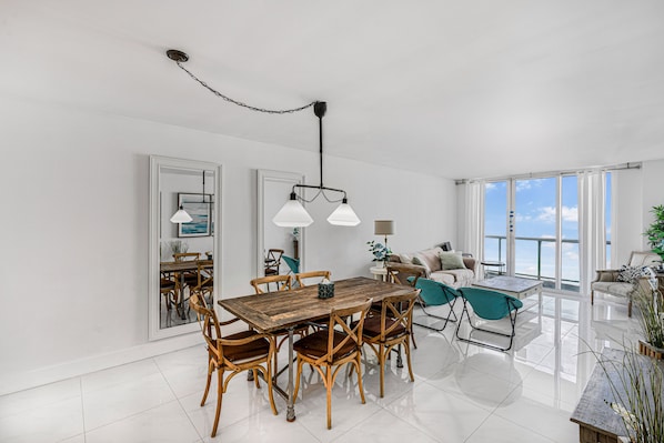 A spacious dining area with a wooden table and chairs, a chandelier, and a view of the sea through large windows. - Beautiful apartment in Sunny Isles Beach! STR-02084 (Sunny Isles Beach)