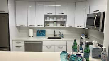 A modern kitchen with white cabinets, a stainless steel refrigerator, a microwave, and a sink.