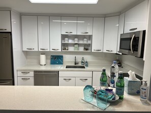 Una cocina moderna con armarios blancos, un refrigerador de acero inoxidable, un microondas y un lavamanos.