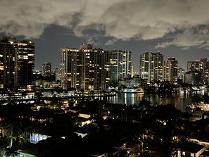 A nighttime cityscape with high-rise buildings and a body of water reflecting the lights. - Beautiful apartment in Sunny Isles Beach! STR-02084 (Sunny Isles Beach)