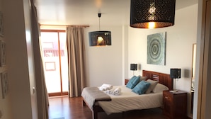 Habitación de hotel con cama, mesitas de noche, alfombra azul, lámpara colgante y un cuadro en la pared.