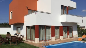 Una casa moderna de dos pisos con piscina, mobiliario exterior y un césped bien cuidado.