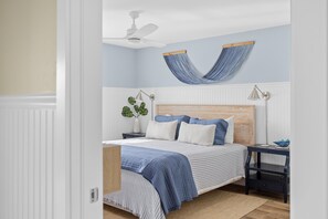 Une chambre à coucher comprenant un lit, une table de chevet, un hamac suspendu, un ventilateur de plafond et une lampe fixée au mur.