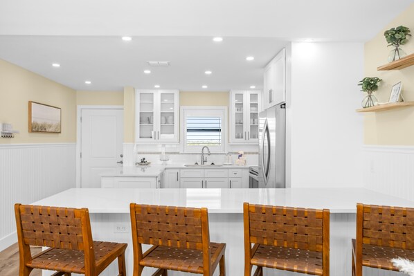 A modern kitchen with white cabinetry, a central island with chairs, and built-in appliances. - Gulf Front Retreat with Modern Coastal Charm (Sanibel)