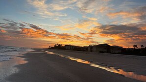 Ein Strand bei Sonnenuntergang, ruhiges Wasser und Gebäude im Hintergrund.