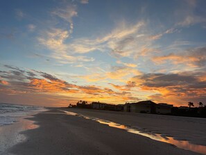 Una playa con un atardecer, aguas tranquilas y edificios al fondo.