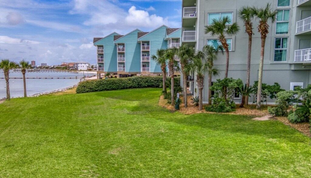 A beachfront hotel with multiple-story buildings, a well-maintained lawn, and palm trees.