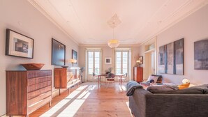 A spacious living area with a wooden floor, a sofa, a dining table with chairs, and a kitchen area with cabinets and a fan. - GuestReady - Ray of Light (Lisbon)