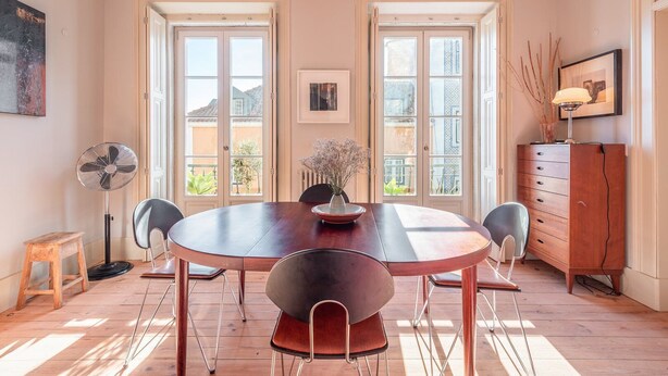 A dining area with a round table, four chairs, a fan, a small stool, and a cabinet with a lamp. - GuestReady - Ray of Light (Lisbon)