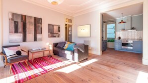 A modern living room with a sofa, a coffee table, and a red and white striped rug. There is a kitchen area with a stove and cabinets. - GuestReady - Ray of Light (Lisbon)