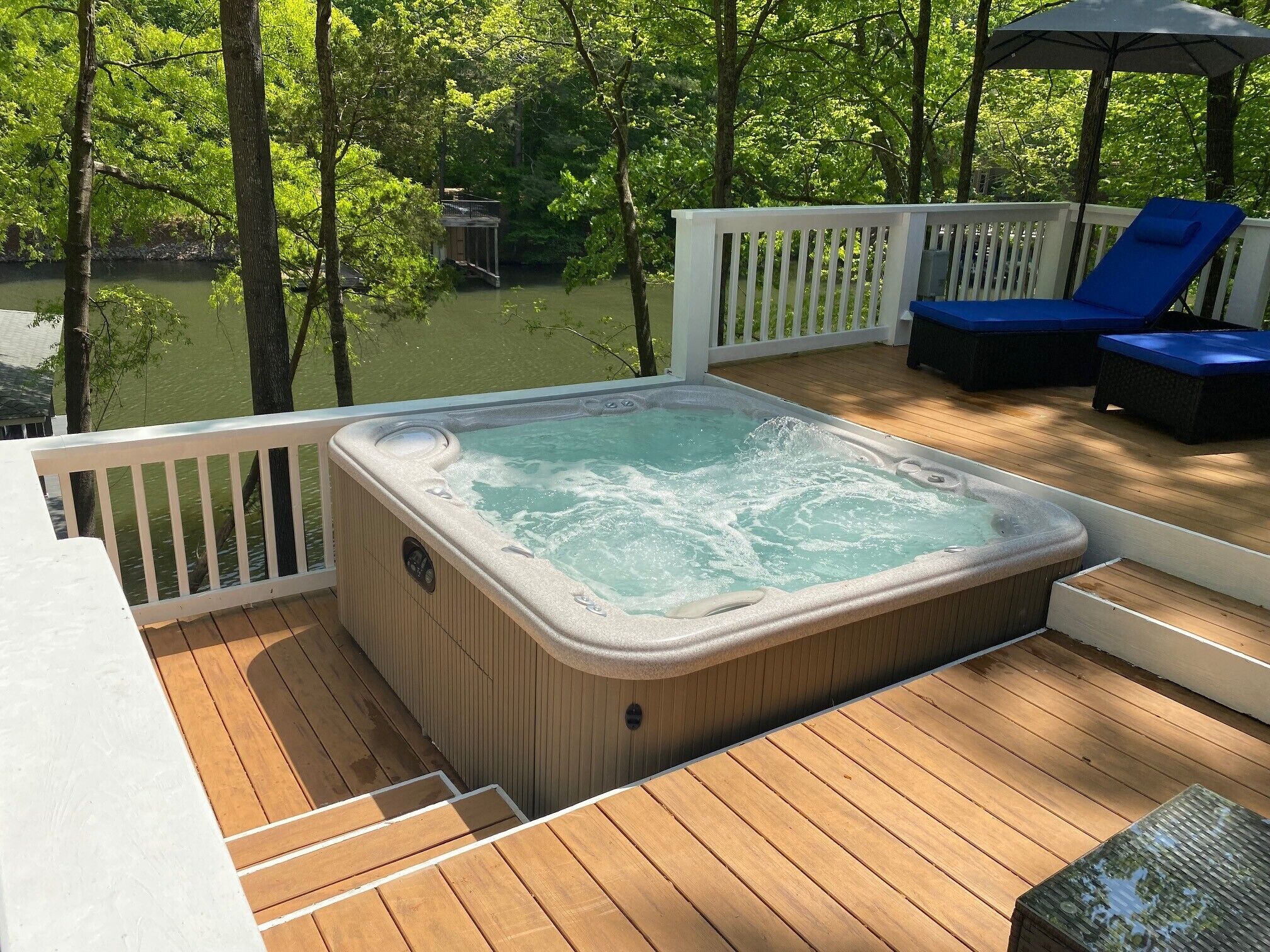 Ein Whirlpool auf einer Holzterrasse mit Blick auf einen See und Bäume.