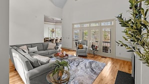 A spacious living room with a grey sofa, a coffee table with a plant, and a large window with a view of the outdoors.