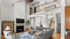 A spacious living room with a fireplace, a grey sofa, a coffee table, and a staircase leading to an upper level.