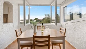 Un espace repas comprenant une table, des chaises et offrant une vue sur le paysage grâce à de grandes fenêtres.