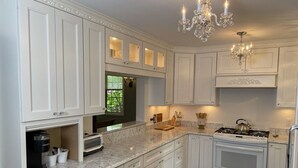 A kitchen with white cabinetry, a built-in oven, a coffee maker, and a chandelier.