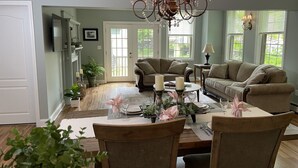 A dining area with a wooden table set for four, surrounded by chairs. There is a chandelier above the table.