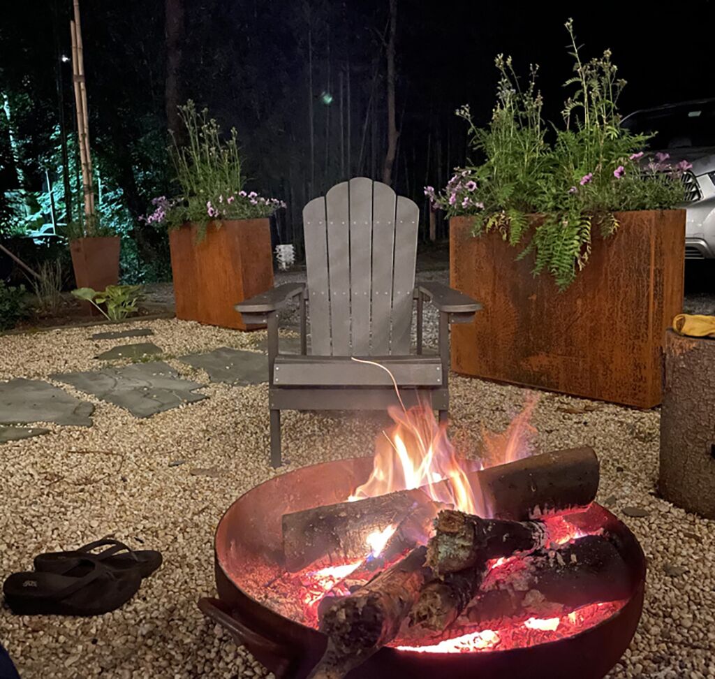 Bålsted med brænde, en træ-Adirondack-stol og krukkeplanter i en have.