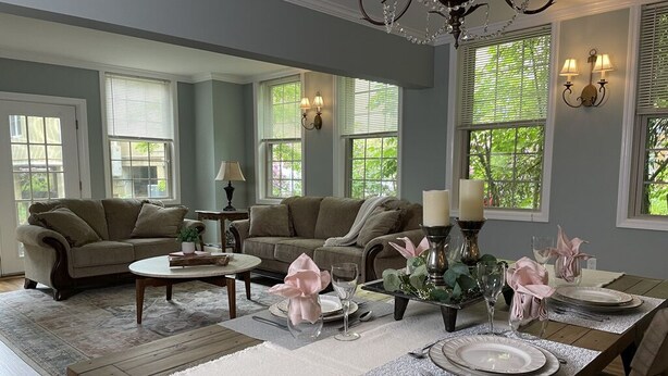 A dining area with a wooden table set for six, surrounded by two sofas and a coffee table.