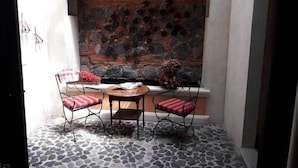 A stone-floored patio with a table and two chairs, a stone wall with a brick section, and a window with a view of the sky. - Casa Antigua (Antigua Guatemala)