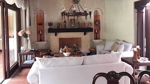 A cozy living room with a fireplace, white sofa, and a chandelier. - Casa Antigua (Antigua Guatemala)
