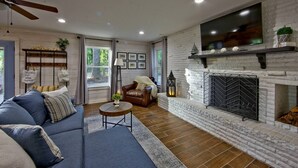 Ein Wohnzimmer mit Kamin, einer Couch, einem Couchtisch und einem an der Wand befestigten Fernseher.