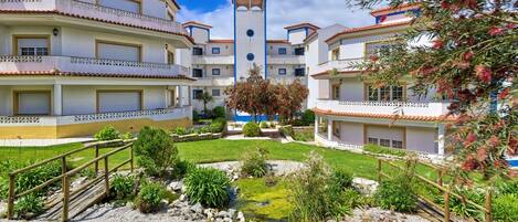 Un patio central con una torre, rodeado de edificios de varios pisos con balcones y un pequeño estanque.