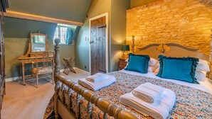 Een slaapkamer met een houten bed, een stenen muur, een houten dressoir en een spiegel.