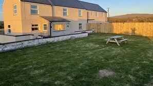 Ein zweigeschossiges Haus mit einem geneigten Dach, einem umzäunten Garten und einem Picknicktisch.